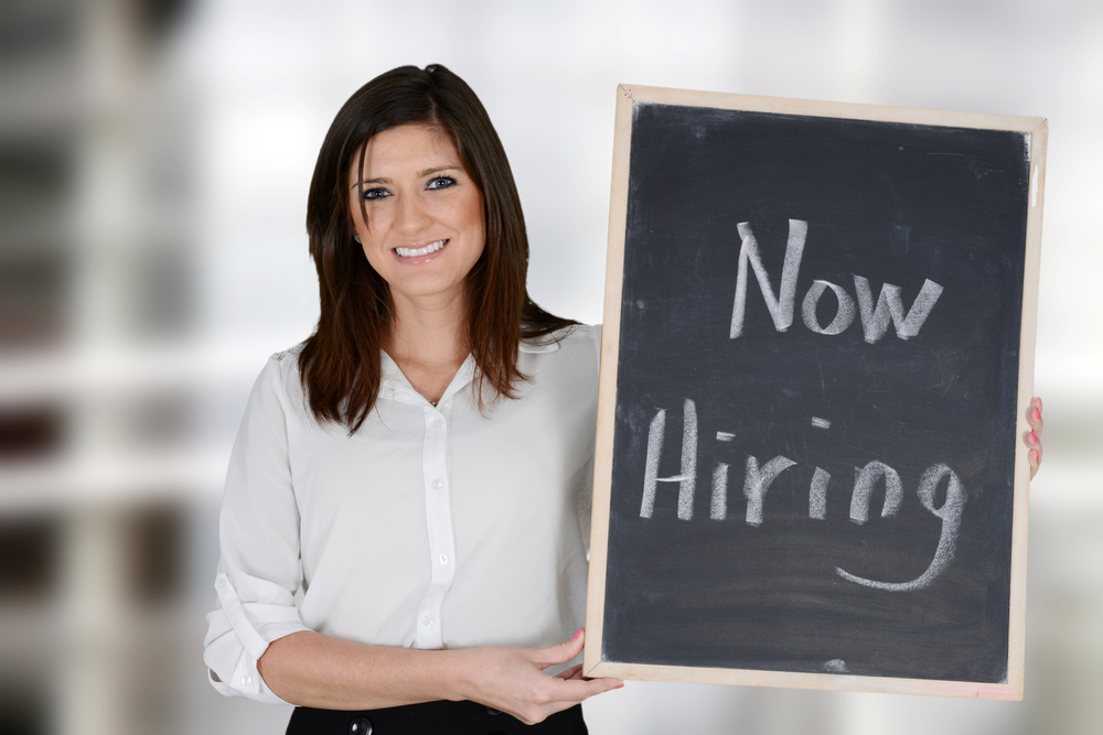 Woman holding "Now Hiring" sign