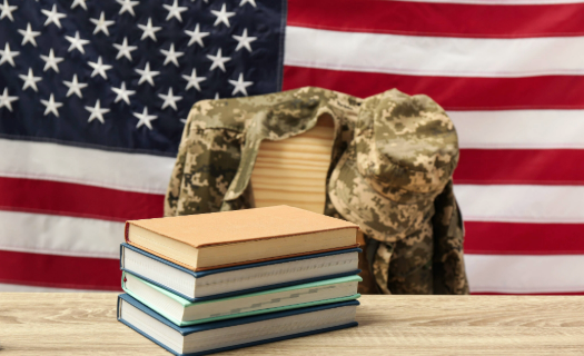 Stack of books with military jacket draped over chair and American flag in the background