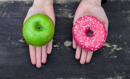 One outstretched palm with a green apple, one outstretched palm with a pink doughnut with sprinkles