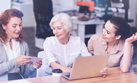 Three women of different ages sitting looking at a laptop