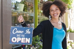 Picture of a woman standing outside a business next to a sign that says 