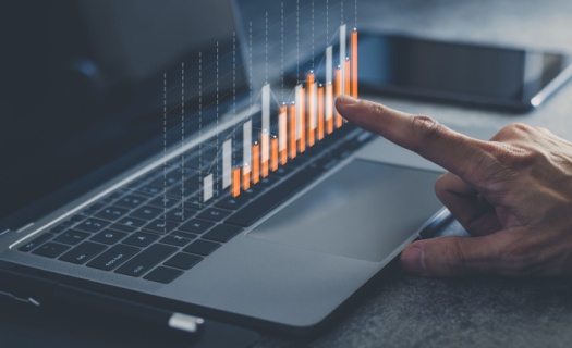 Hand point at bar chart that is floating above laptop keyboard