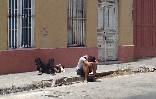Two young men on sidewalk - one lying on his back and the other one sitting with head in arms