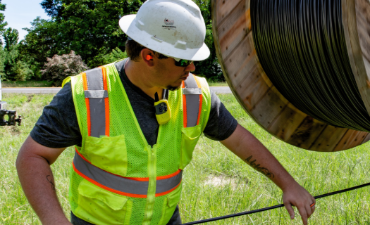 Man in safety vest and hard hat pulling cable from a large spool