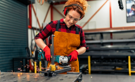 Young woman in a shop grinding metal with a saw