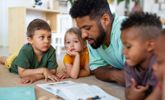 An adult and four children reading together on the floor in an at-home daycare.
