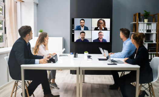 Professionals sitting at a conference room table and interacting with colleagues on a screen during a video call.