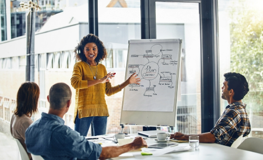 A woman in a conference room teaching from a large paper flip-chart.