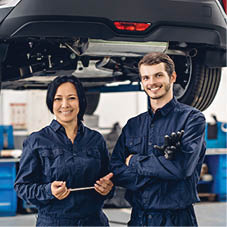 Auto car repair service center. Two happy mechanics - man and woman standing by the car