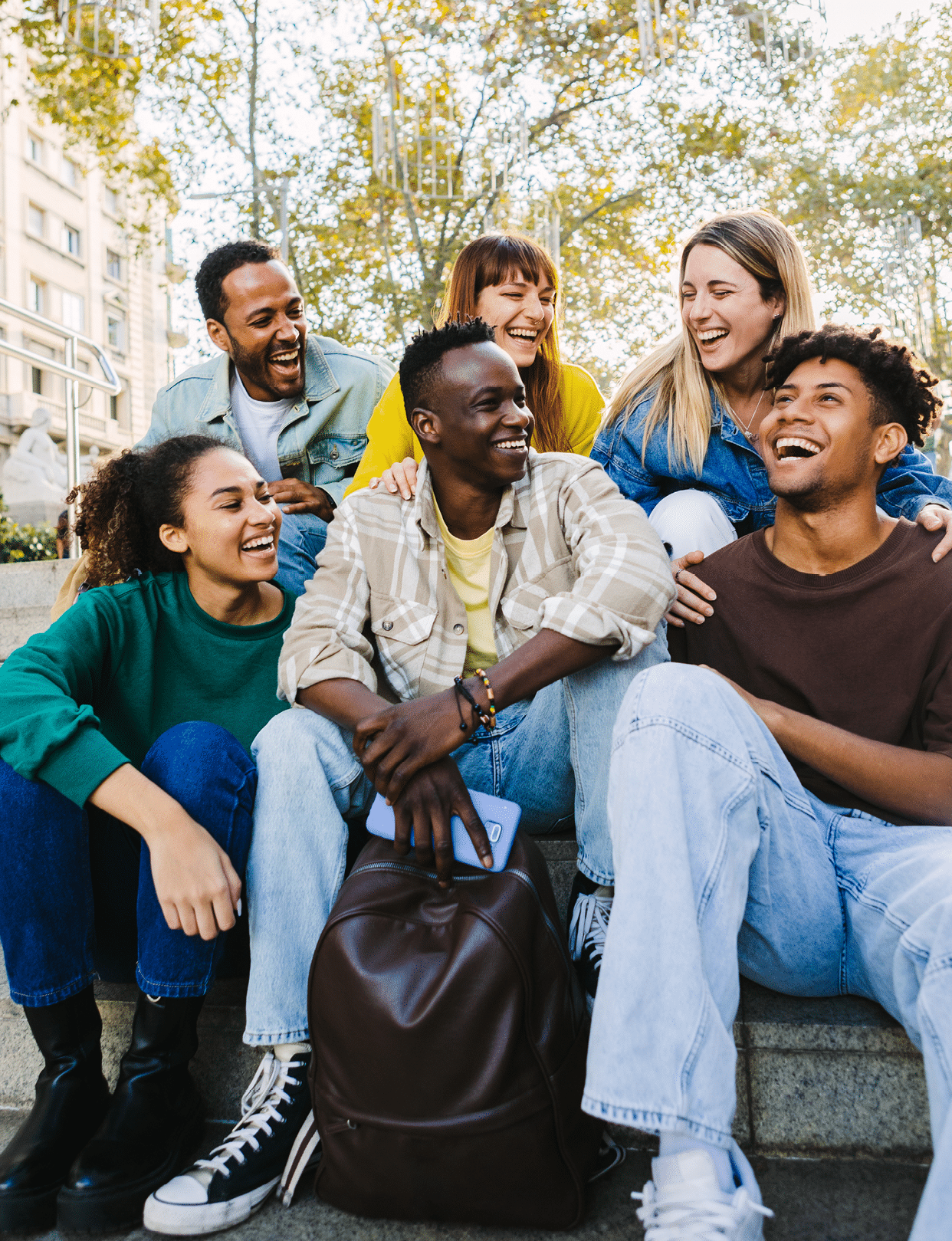 Vertical shot of happy multi-ethnic group of young hipster diverse student friends having fun together while hanging out sitting together outdoors. Friendship concept